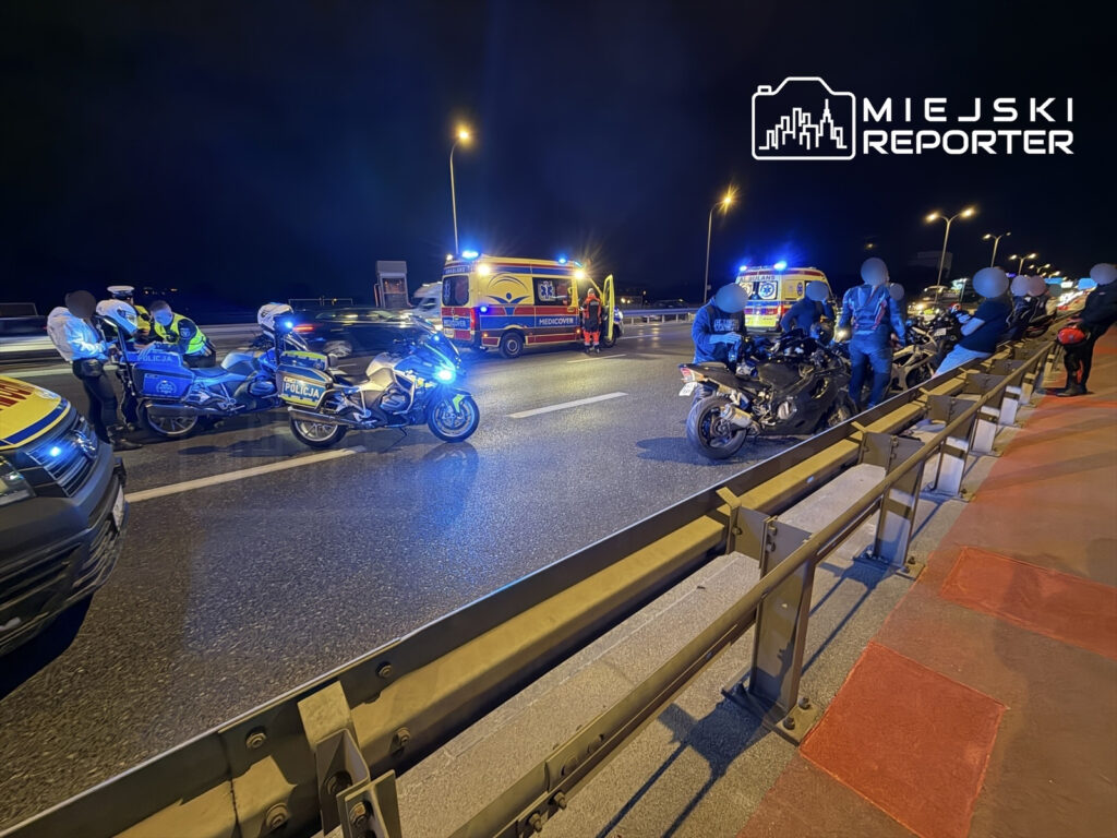 Policjanci w mundurach rozmawiają z motocyklistami obok zderzenia trzech motocykli na ruchliwej drodze nocą.