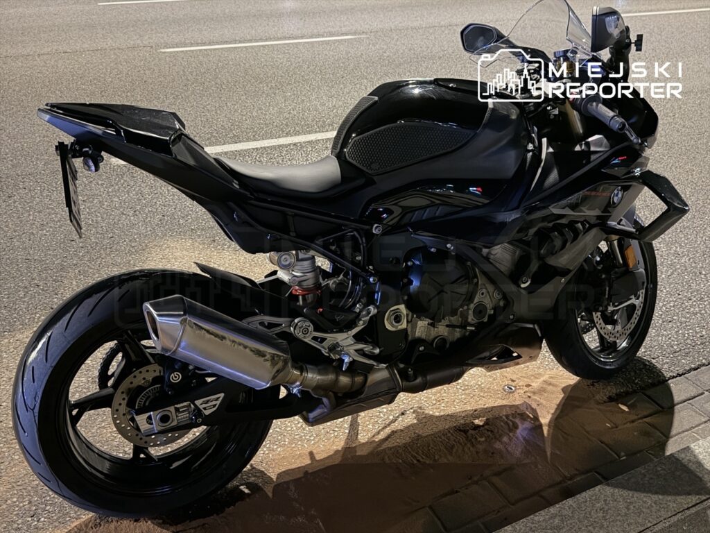 Czarny motocykl sportowy zaparkowany na poboczu drogi, z widocznym wydechem i detalami konstrukcyjnymi.