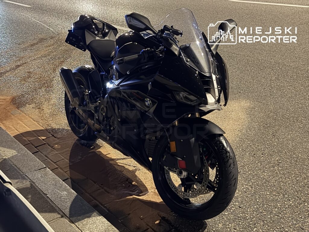 Czarny motocykl sportowy zaparkowany na mokrej nawierzchni, w tle widoczne oświetlenie uliczne.