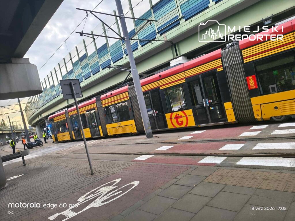 Motocyklista na drodze obok tramwaju, przy którym stoją funkcjonariusze w odblaskowych kamizelkach.