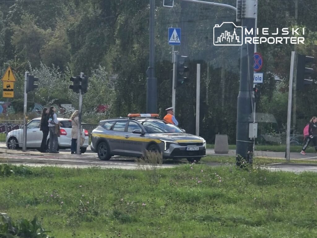 Grupa osób rozmawia obok białego samochodu, a w tle widoczny radiowóz z włączonymi sygnałami świetlnymi. Awaria tramwajów.