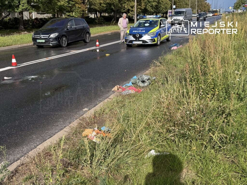 Na jezdni, obok policyjnego radiowozu, leżą porozrzucane ubrania oraz znaki ostrzegawcze, świadczące o potrąceniu.