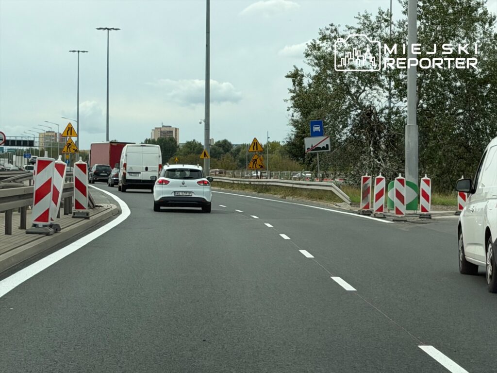 Kierowcy poruszają się dwoma pasami lokalnymi na trasie S8, mijając znaki drogowe i bariery ochronne.