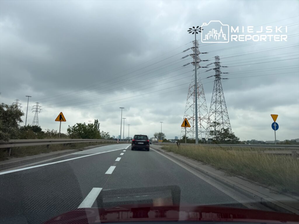 Droga S8 z oznaczeniami drogowymi i samochodami w ruchu, w tle widoczne słupy wysokiego napięcia.