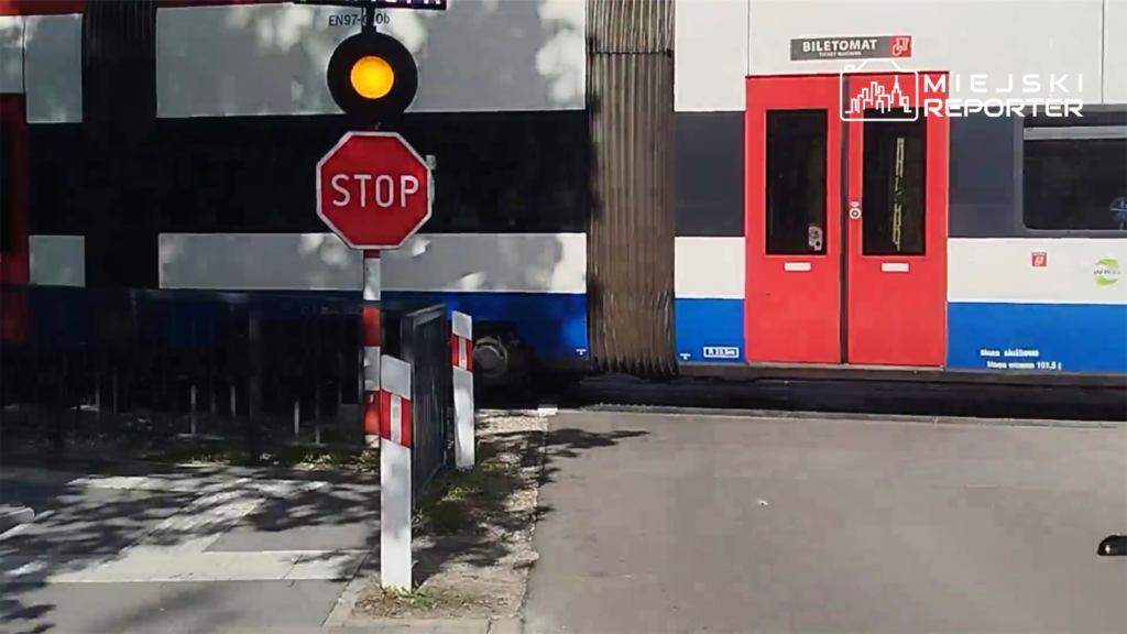 Czerwony biletomat obok przystanku, sygnalizator świetlny pokazujący czerwone światło, znak STOP na drodze.