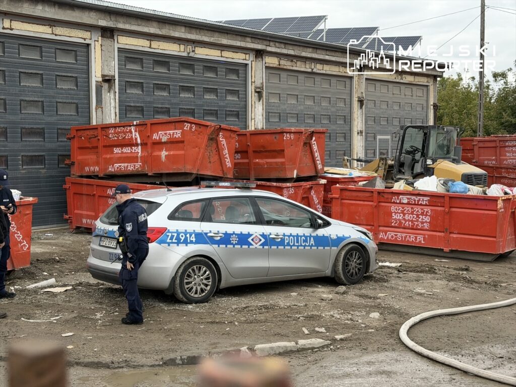 Policjanci w mundurach prowadzą działania przy czerwonych kontenerach na terenie zakładu na Płochocińskiej.
