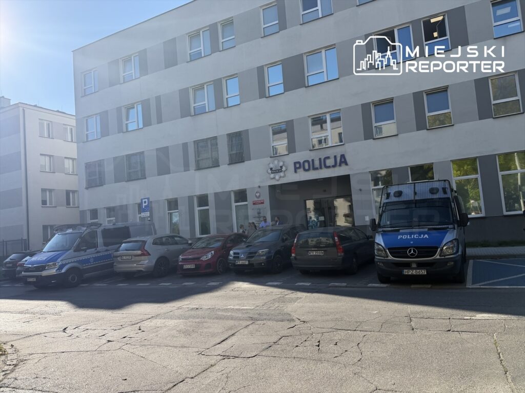 Budynek komisariatu z napisem „POLICJA” i radiowozami zaparkowanymi przed wejściem.