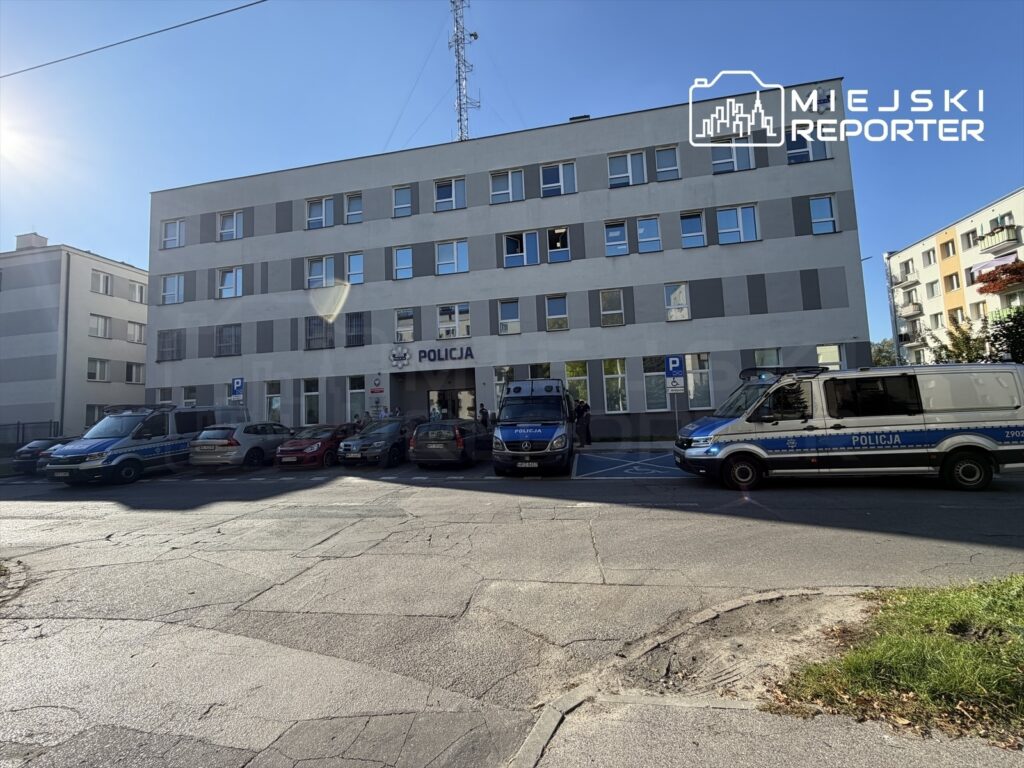 Budynek komisariatu policji z napisem „POLICJA”, przed wejściem zaparkowane radiowozy i samochody osobowe.