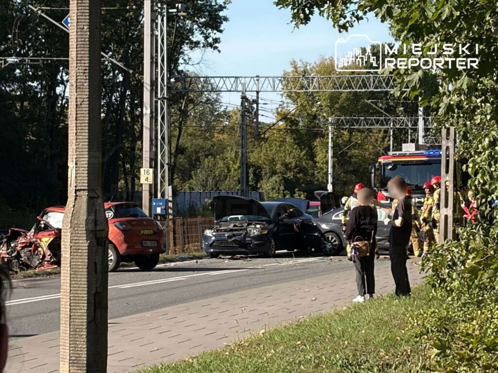 Uszkodzone samochody po zderzeniu na drodze, obok straż pożarna i osoby stojące na chodniku