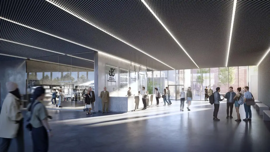 Grupa osób przebywa w nowoczesnym wnętrzu muzeum z przeszklonymi ścianami, rozmawiając i zwiedzając.