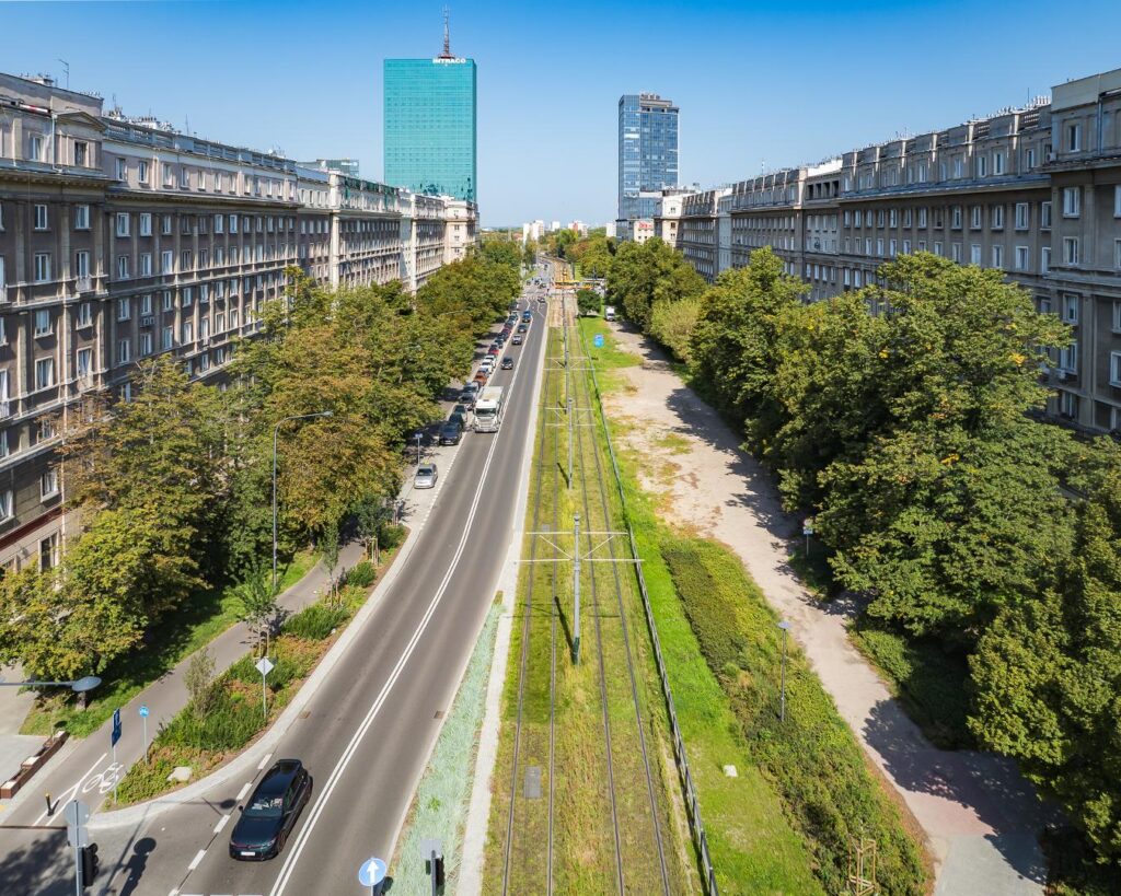 Ulica z torowiskiem tramwajowym, samochodami i drzewami między rzędami kamienic, widziana z góry