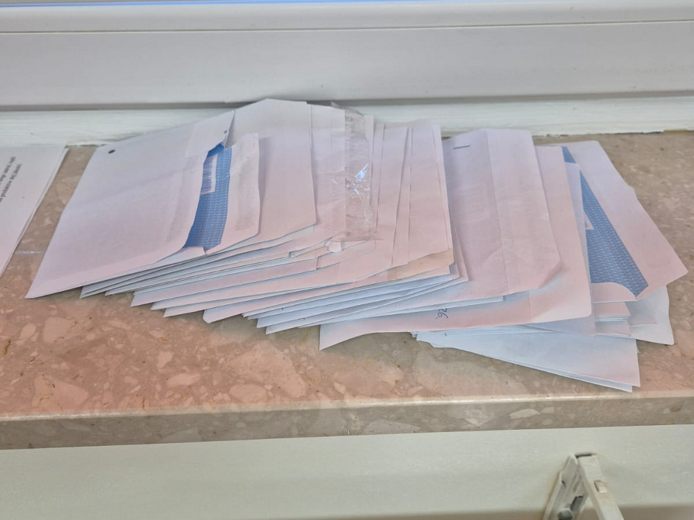 Stos papierowych kopert rozłożony na parapecie z kamiennym blatem, przy białej ścianie.