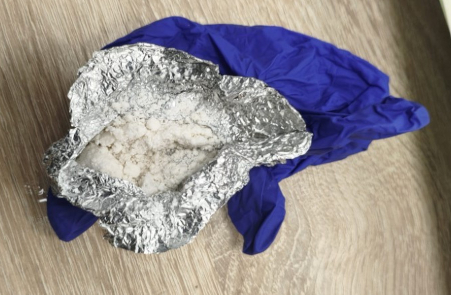 Biały proszek w rozłożonej folii aluminiowej leżącej na niebieskiej rękawiczce na drewnianej podłodze.