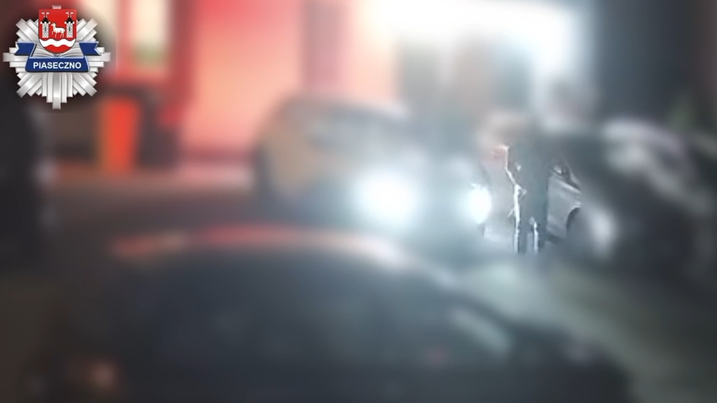 Rozmazany kadr nocą: samochód z rozbitą boczną szybą stoi przy oświetlonej ulicy.