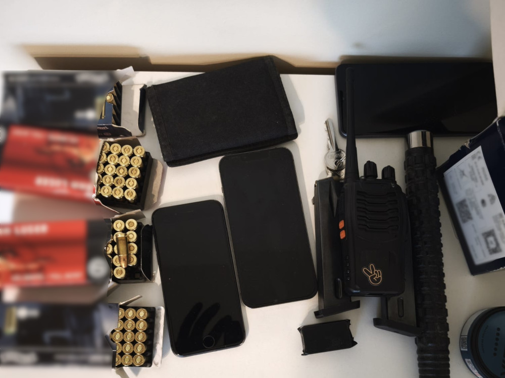 Telefony, radiotelefony, akcesoria i pudełka z amunicją rozłożone na białej powierzchni