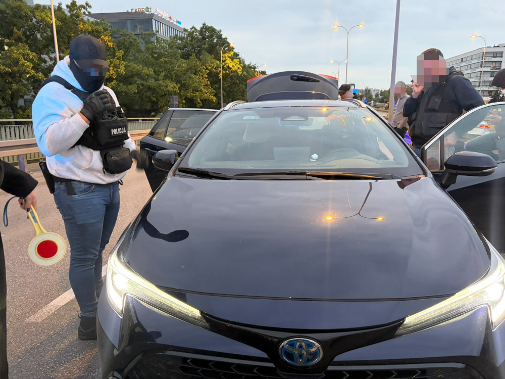 Policjanci kontrolują samochód Toyota na ulicy, przy otwartym bagażniku i drzwiach pojazdu.