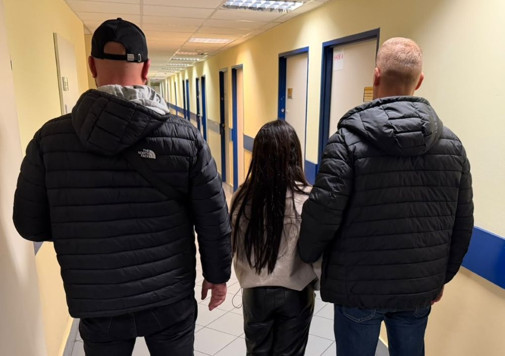 Dwóch mężczyzn idzie korytarzem po bokach młodej kobiety, trzymając ją za ręce.