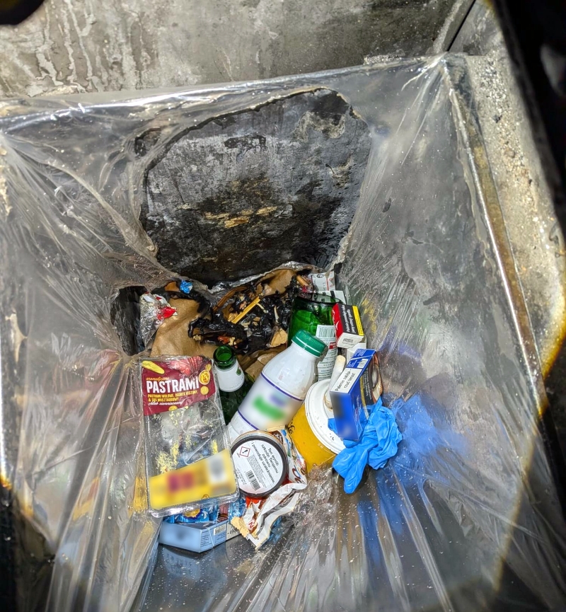 Wnętrze metalowego pojemnika wyłożonego folią, wypełnione śmieciami, opakowaniami i zużytymi rękawiczkami.
