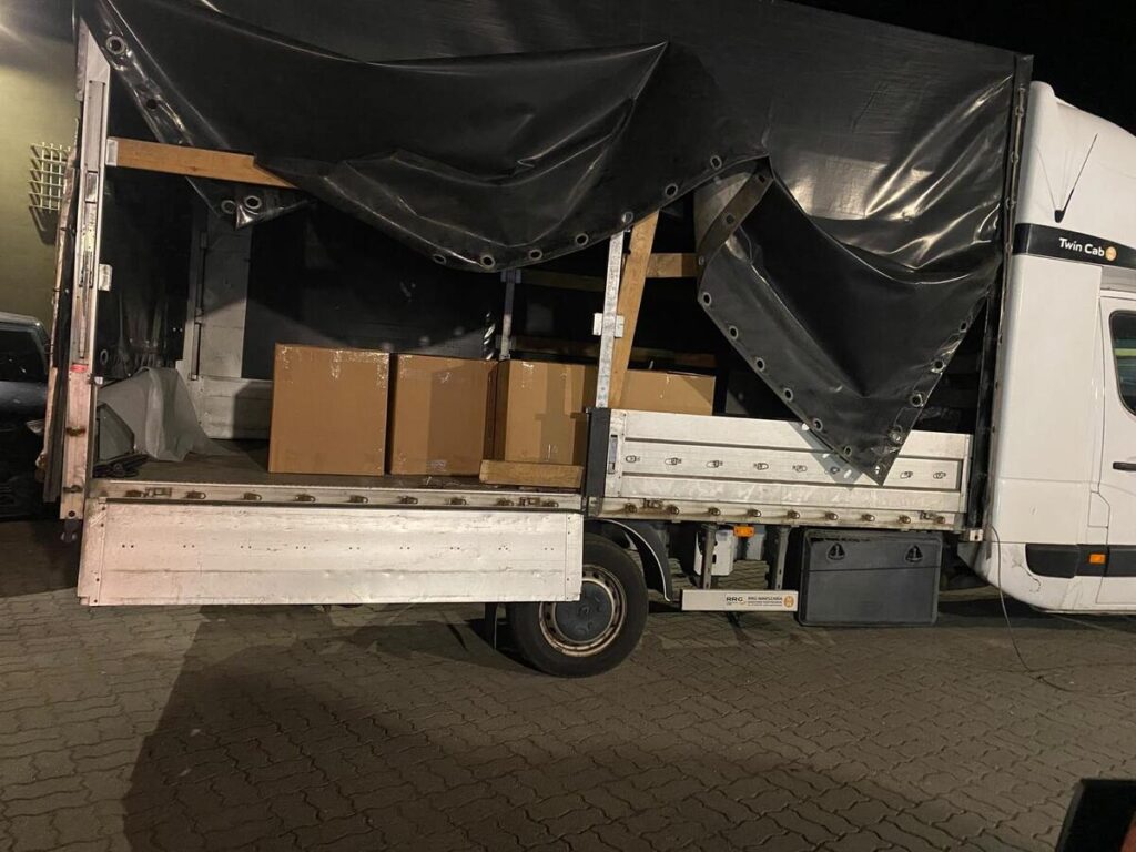 Kartony załadowane na ciężarówkę z odsuniętą plandeką na oświetlonym parkingu