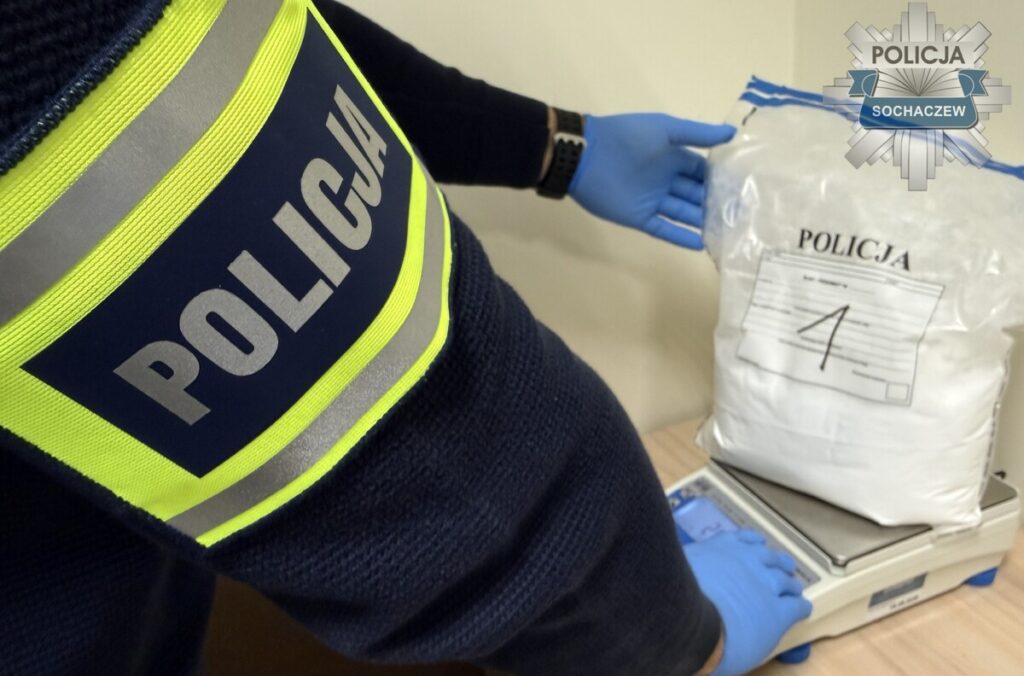 Policjant w rękawiczce waży na wadze zabezpieczony worek z napisem „POLICJA” i numerem 4.