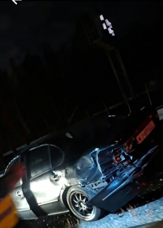 Uszkodzony srebrny samochód z wgniecionymi drzwiami i rozbitym bokiem stoi nocą przy drodze.
