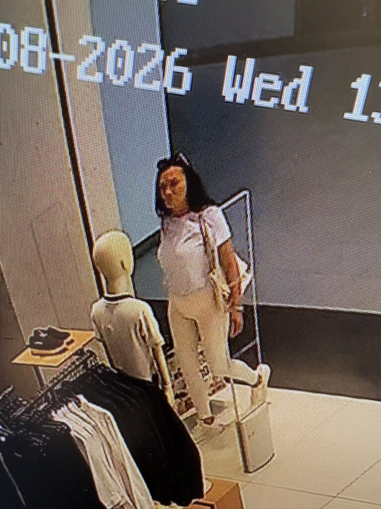 Kobieta w jasnym stroju stoi przy manekinie i wieszakach z ubraniami w sklepie odzieżowym