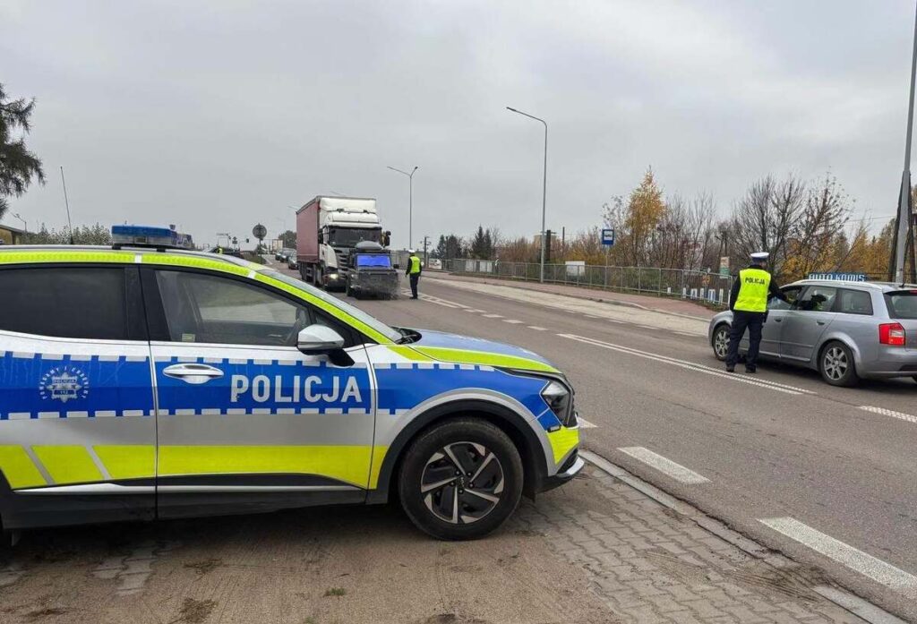 Radiowóz policyjny blokuje część drogi, a funkcjonariusze kontrolują ciężarówkę i samochód osobowy.