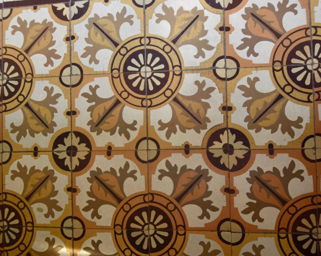 Dekoracyjne ceramiczne płytki z powtarzającym się wzorem kwiatów i geometrycznych rozet w odcieniach beżu i brązu.