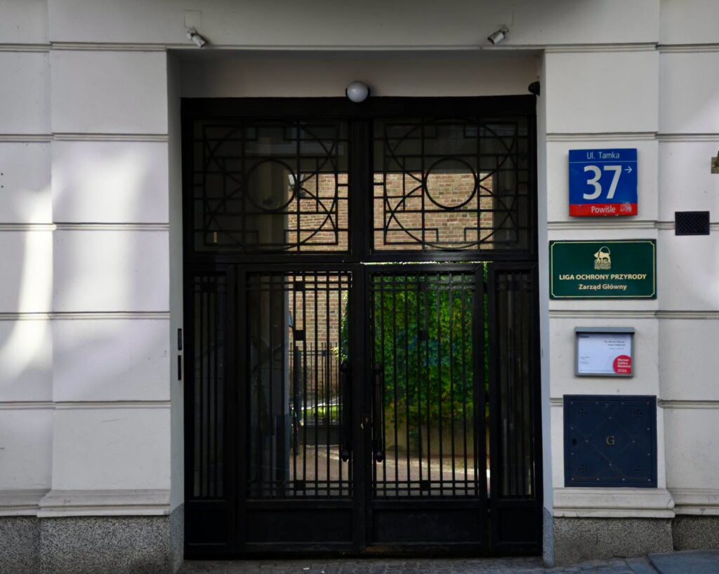 Czarna metalowa brama wejściowa przy tabliczce z adresem „ul. Tamka 37” i szyldem Ligi Ochrony Przyrody.