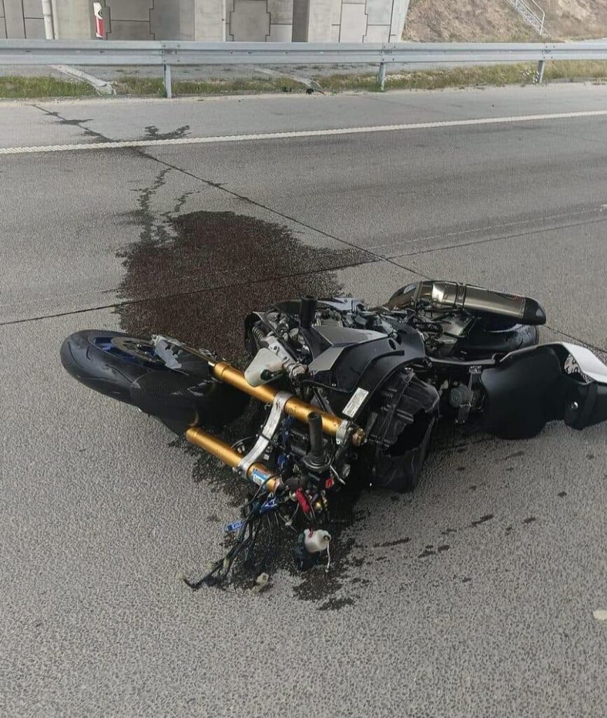 Przewrócony motocykl leży na jezdni, obok rozlanej cieczy i śladów wycieku.