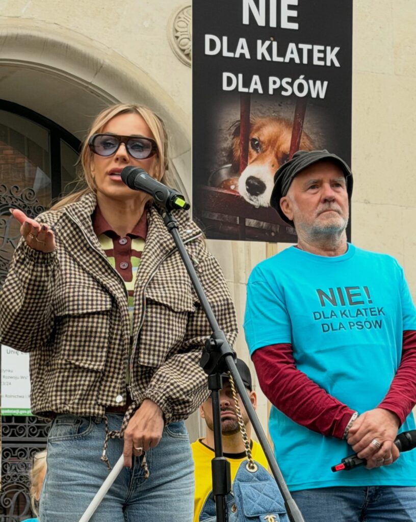 Kobieta przemawia do mikrofonu podczas protestu, obok mężczyzna w koszulce „NIE! DLA KLATEK DLA PSÓW” i plakat z psem za