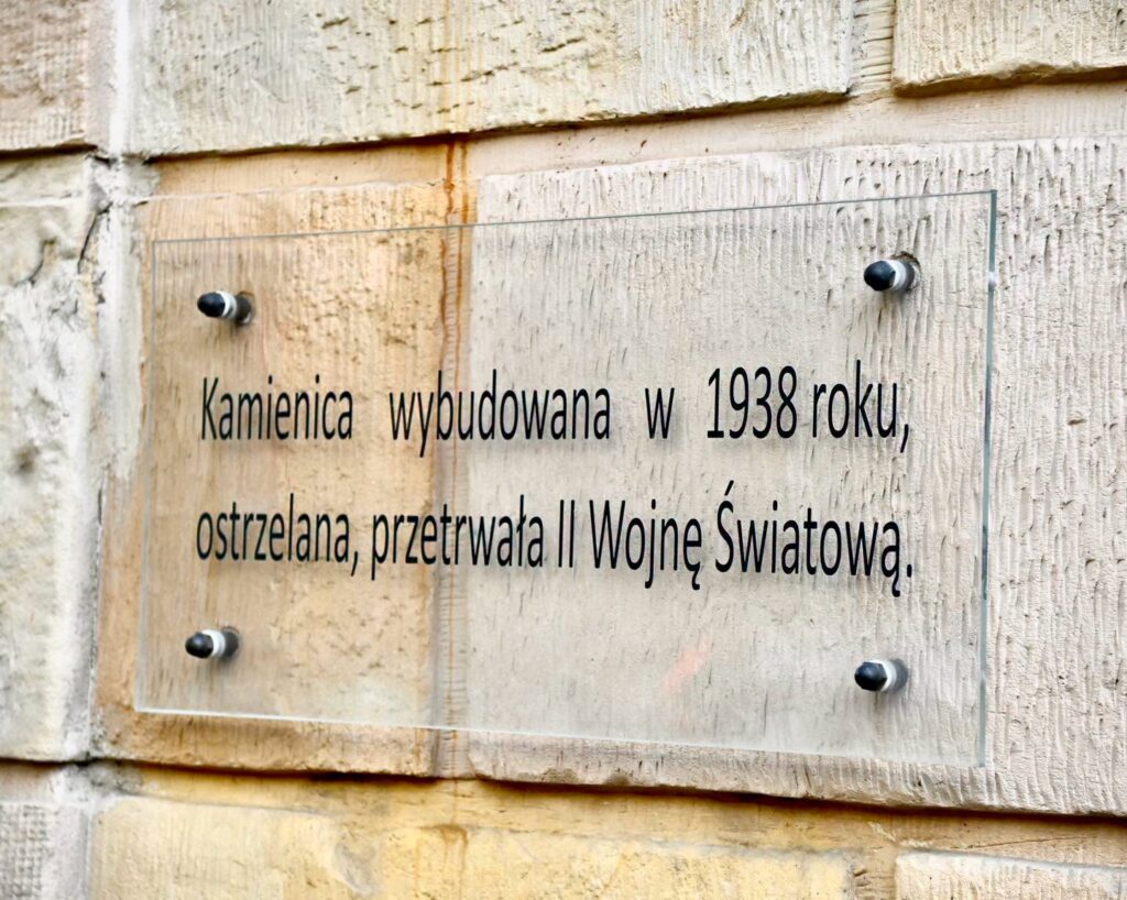 Tablica na kamiennej ścianie informuje: „Kamienica wybudowana w 1938 roku, ostrzelana, przetrwała II Wojnę Światową”.