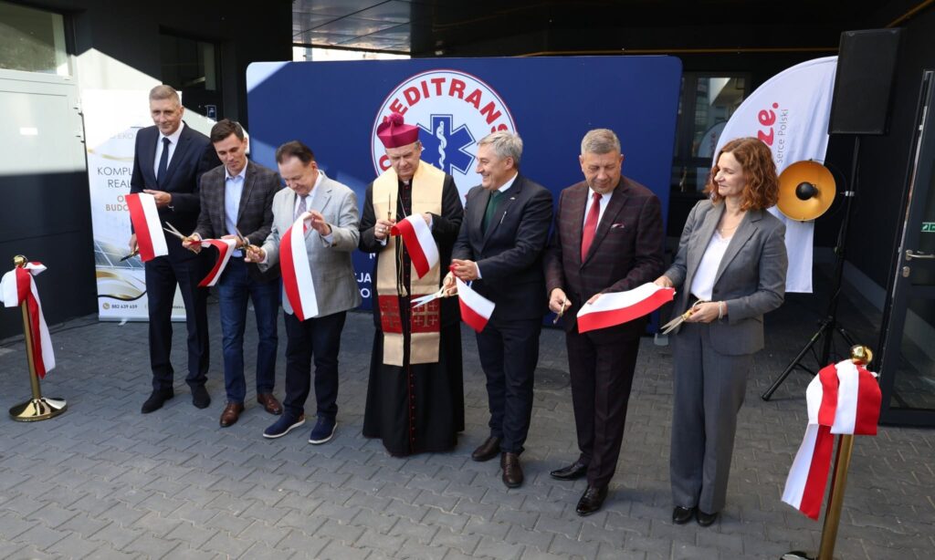 Grupa osób przecina biało-czerwone wstęgi podczas uroczystości przed wejściem do budynku, na tle logo „MEDITRAN”.