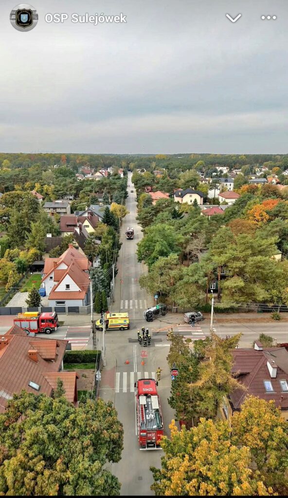 Strażacy i wozy ratownicze na skrzyżowaniu wśród domów jednorodzinnych, widok z góry.