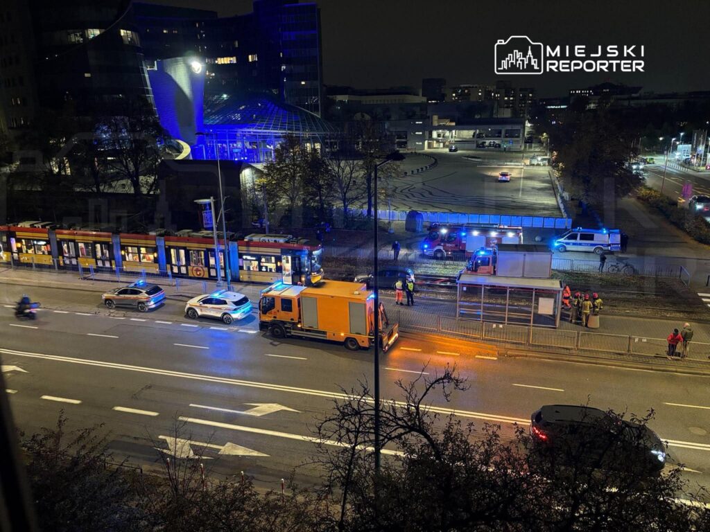 Służby ratunkowe i tramwaj przy torowisku, nocą na oświetlonej ulicy.