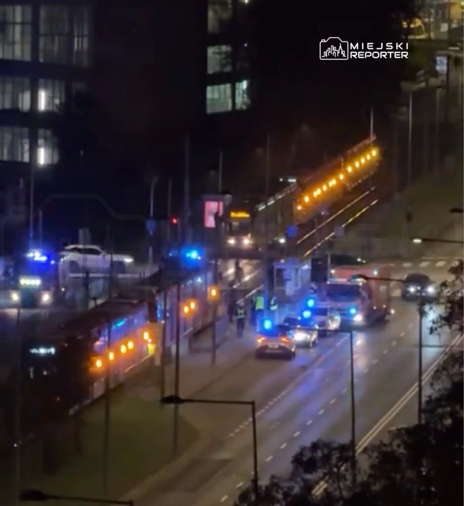 Służby ratunkowe i pojazdy z niebieskimi światłami na nocnej ulicy obok tramwajów i wiaduktu