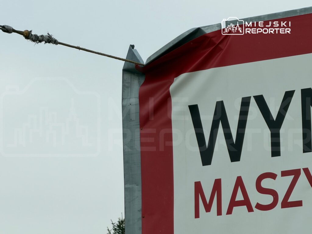 Fragment biało-czerwonego baneru z widocznym napisem „WY… MASZ…” zawieszony na metalowej konstrukcji na zewnątrz.