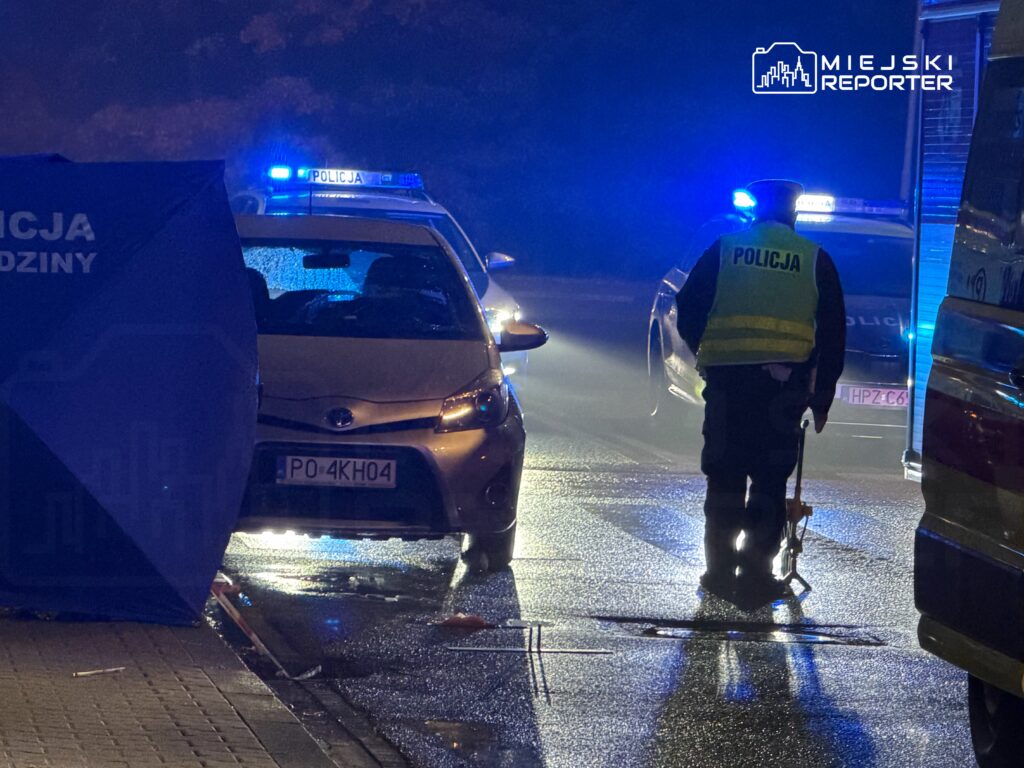 Radiowóz policyjny z włączonymi niebieskimi światłami stoi nocą na ulicy; widoczny napis „POLICJA”.
