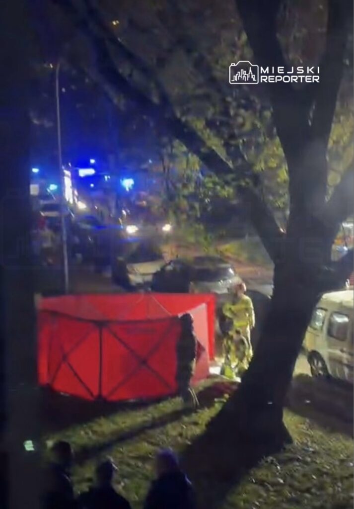 Ratownicy w odblaskowych strojach działają nocą przy czerwonym namiocie obok zaparkowanych pojazdów