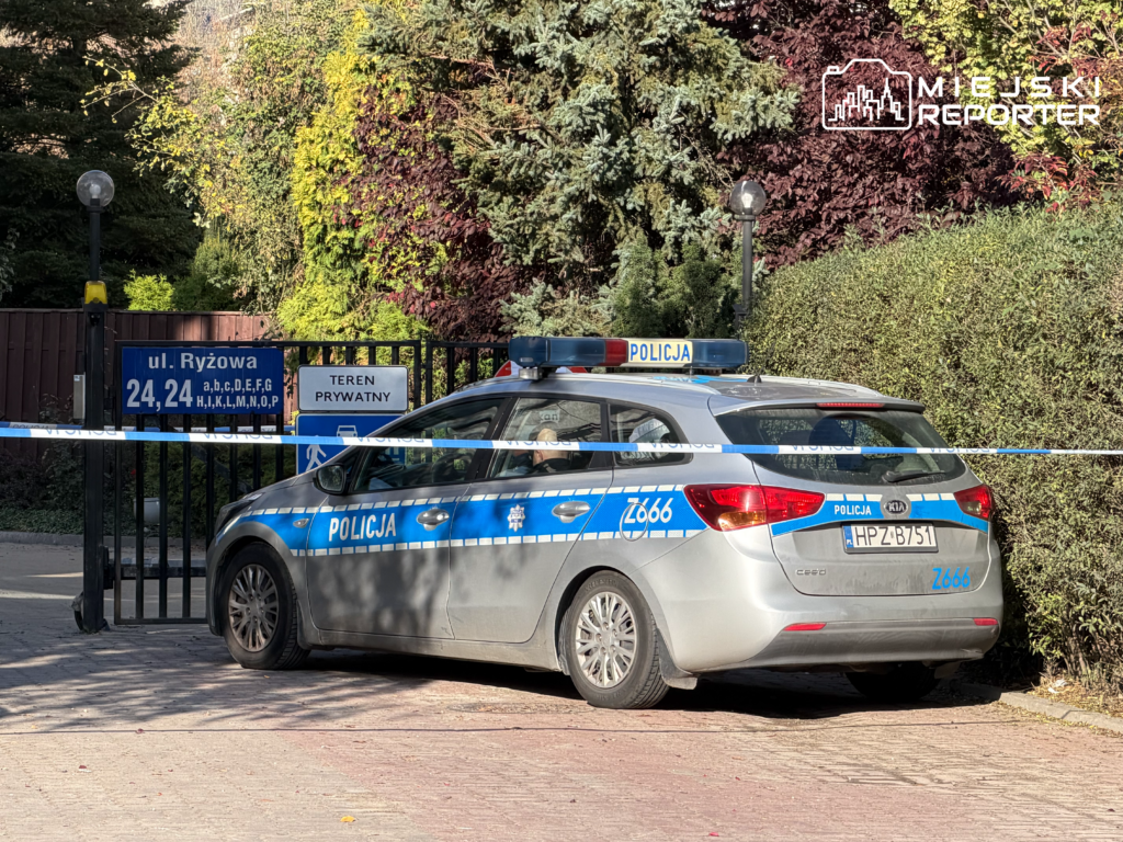 Oznakowany radiowóz stoi za policyjną taśmą przy bramie posesji z tablicami „ul. Ryżowa” i „Teren prywatny”.