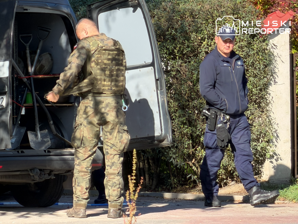 Funkcjonariusz w mundurze kamuflażowym sięga do otwartego samochodu dostawczego, obok stoi policjant w granatowym mundurze.