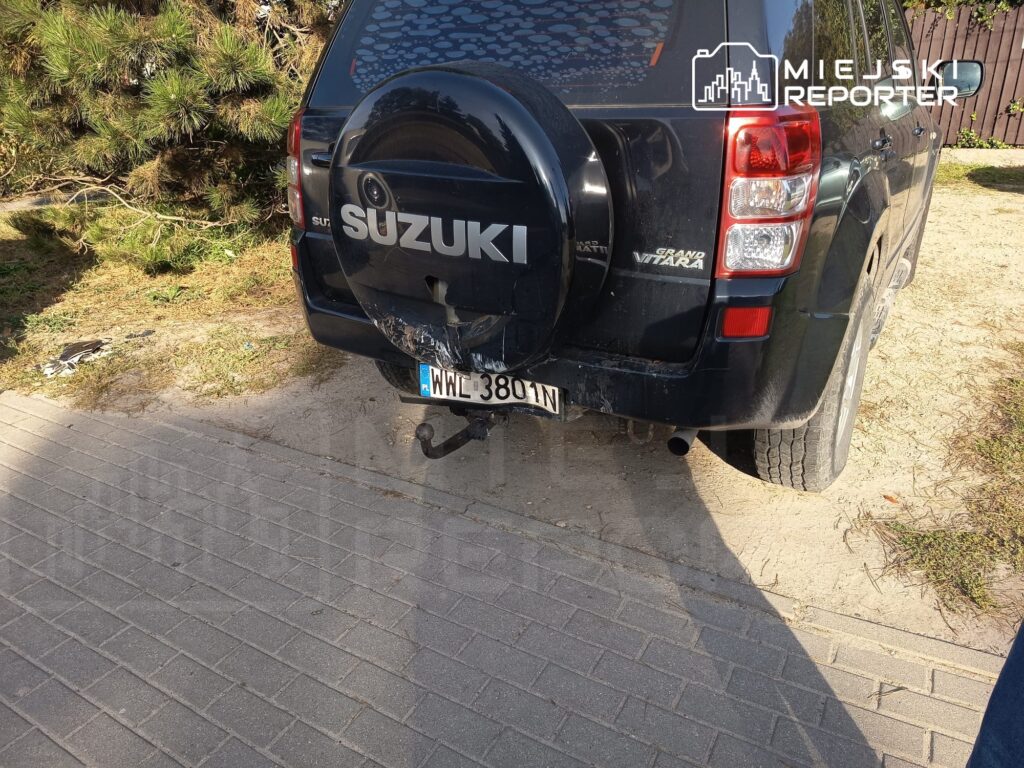 Tył czarnego Suzuki Grand Vitara z widocznym uszkodzeniem zderzaka i tablicą rejestracyjną przy chodniku.