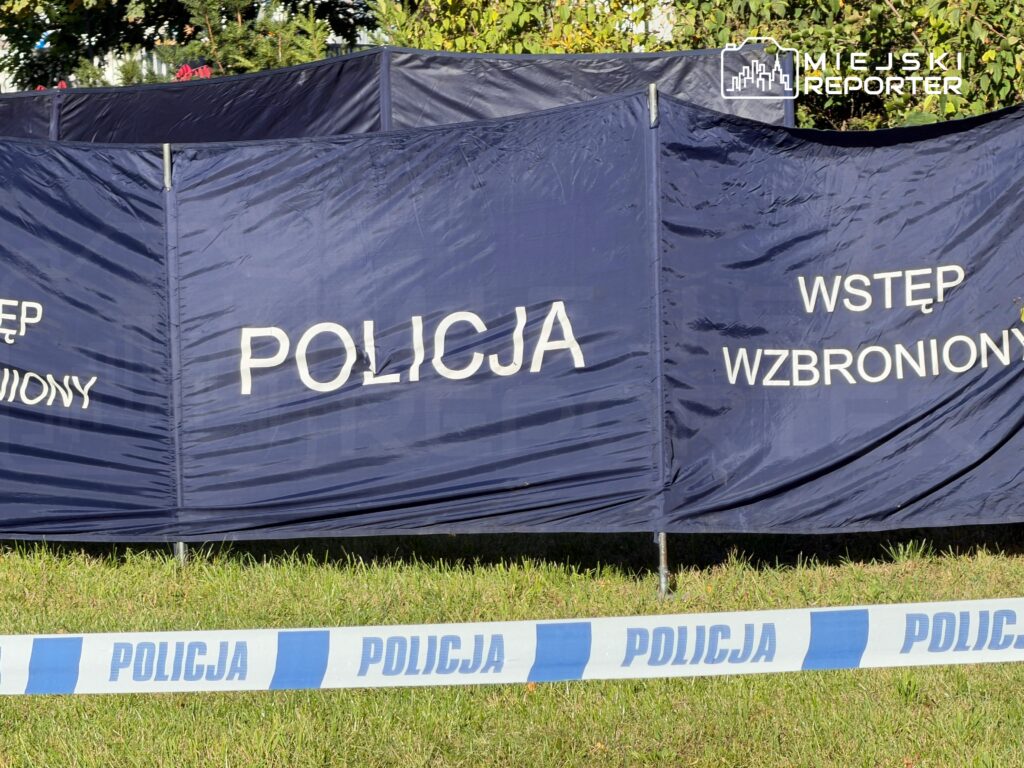 Granatowe policyjne parawany z napisami „POLICJA” i „WSTĘP WZBRONIONY” oraz taśma policyjna na trawie.