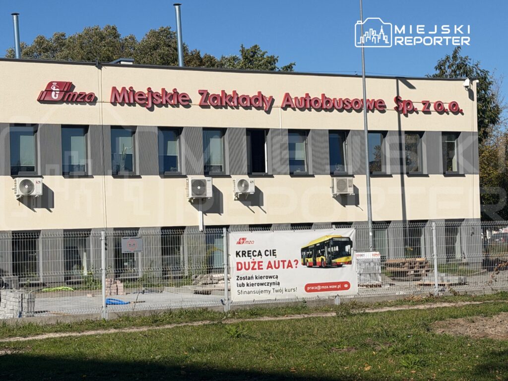 Budynek Miejskich Zakładów Autobusowych z szyldem „Łomża Miejskie Zakłady Autobusowe sp. z o.o.” za ogrodzeniem.
