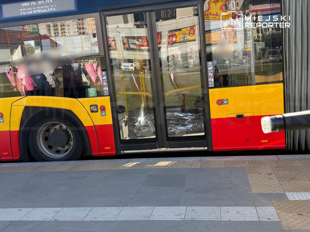 Żółto-czerwony autobus miejski z otwartymi drzwiami stoi przy chodniku; na podłodze przy wejściu leżą rozbite szkło i