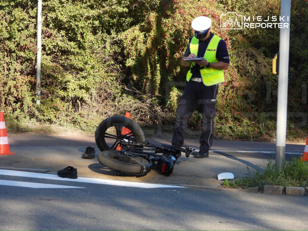 Policjant w odblaskowej kamizelce sporządza notatki obok przewróconego roweru na jezdni.