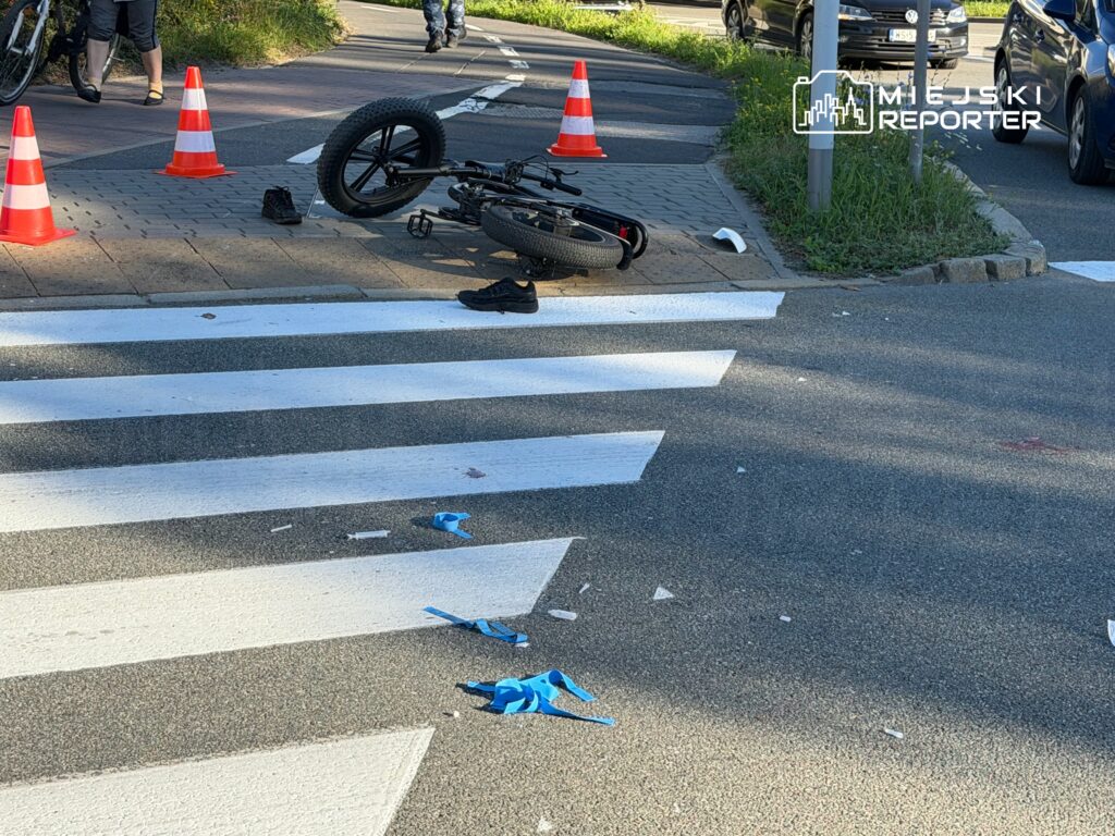 Rozbity rower leży przy przejściu dla pieszych, otoczony pachołkami i porozrzucanymi elementami wyposażenia.