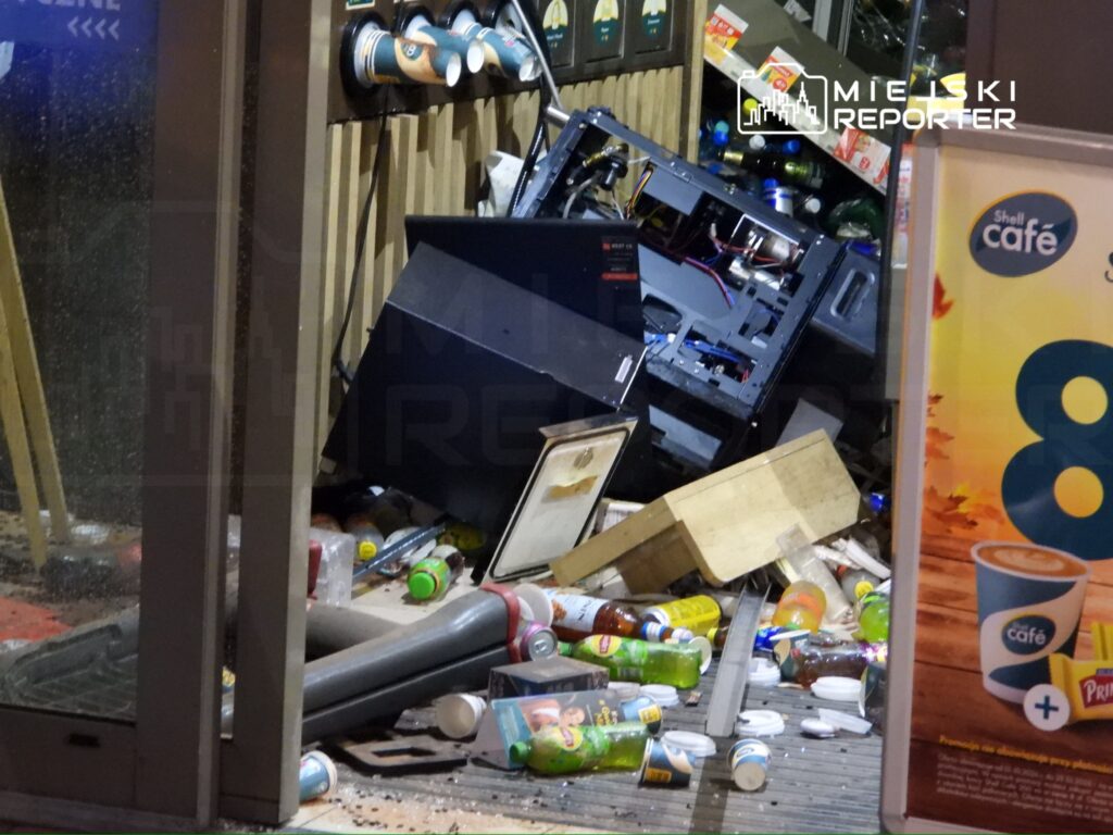 Przewrócone urządzenia i porozrzucane napoje wewnątrz zniszczonego sklepu z kawą; witryna jest uszkodzona.