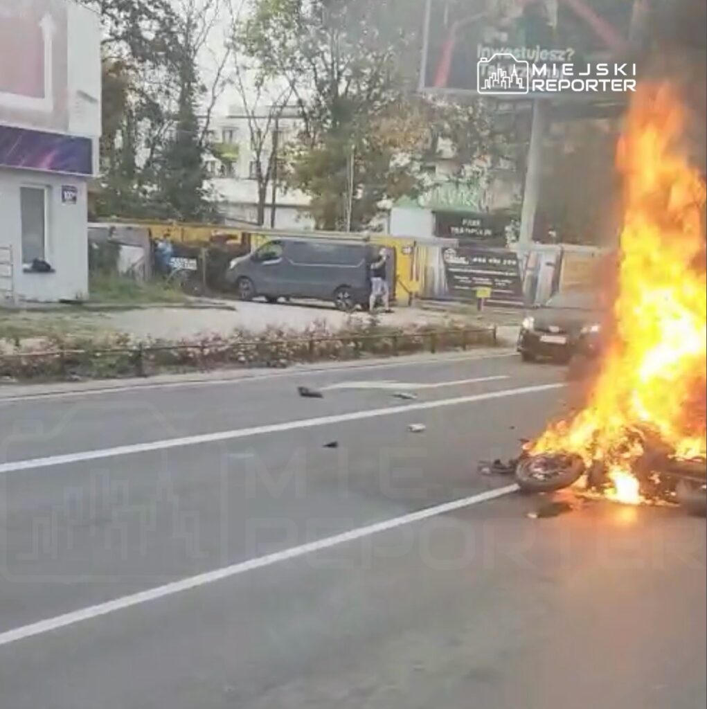 Płonący motocykl leży na jezdni, a wokół niego widać rozrzucone fragmenty pojazdu.