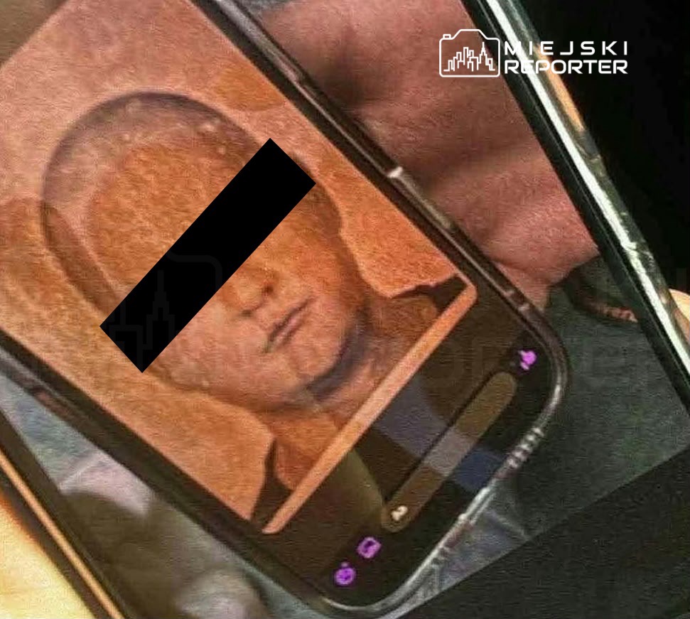 Smartfon z wyświetlonym zdjęciem twarzy mężczyzny, którego oczy zasłania czarny pasek.